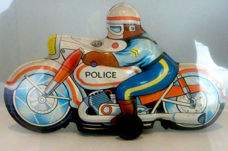 foto de una moto de juguete antigua, con colores primarios, naranja, azul, amarillo y marrón